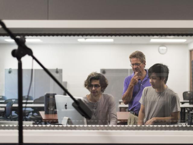 Three students in a sound booth working with recording equipment