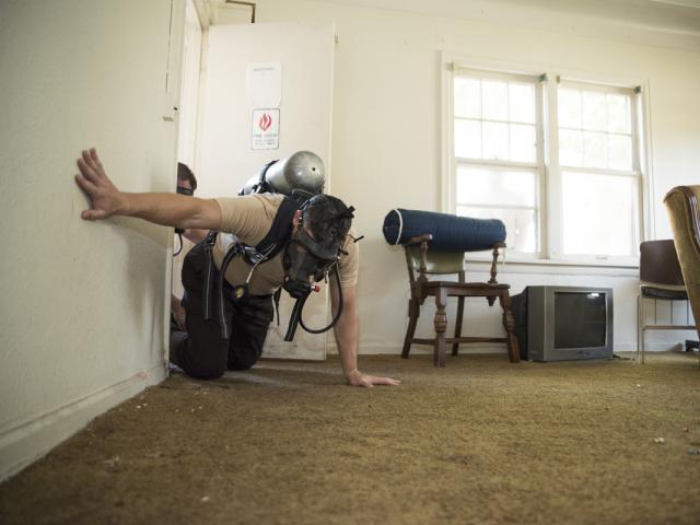 Sheriff’s Corrections Academy student crawling in a house with a gas mask on.