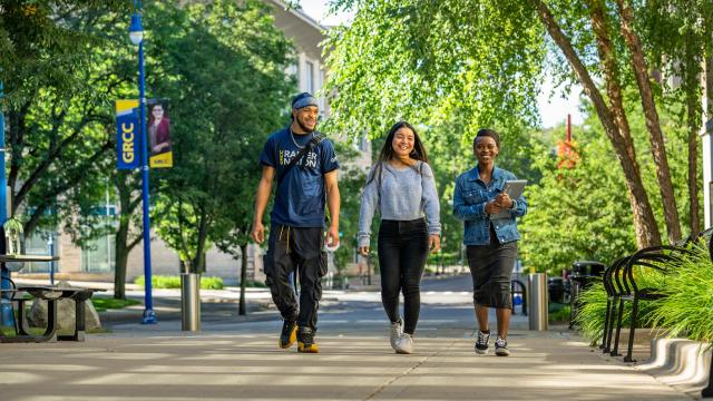 Three students walk down a path at GRCC, smiling.