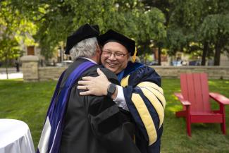 Dr. Lepper hugs someone. They both are wearing academic regalia. 
