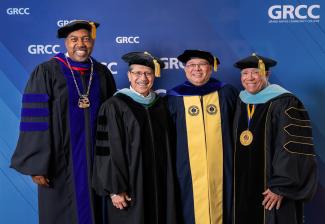 Dr. Lepper poses with three other people, all wearing academic regalia, in front of a GRCC banner.