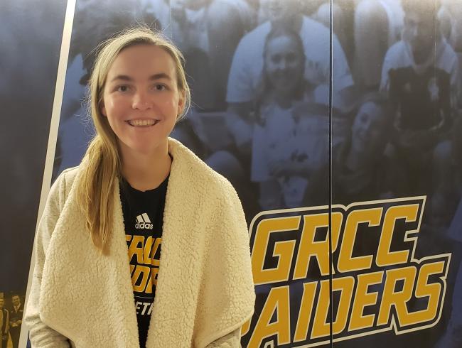 Amanda Glaza standing in front of a GRCC Raiders Logo.