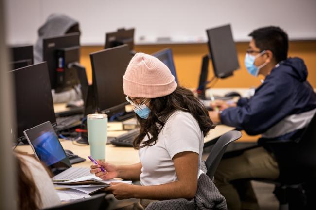 Students in face coverings working in a classroom on computers