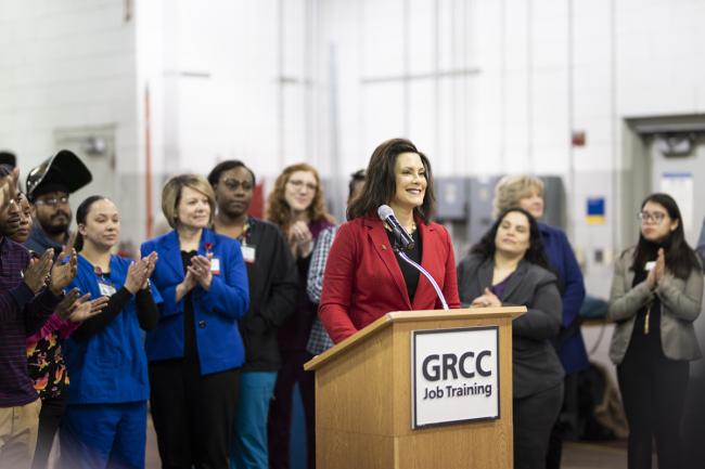 Governor Gretchen Whitmer standing at a podium in the Tassell M-TEC, surrounded by students, faculty and community partners.