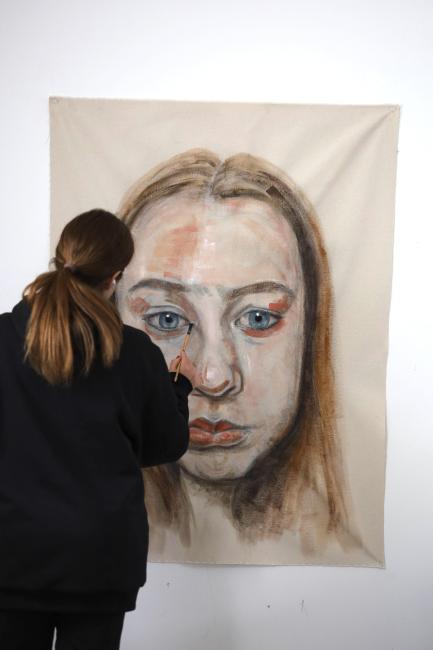 Erin Reinholz paints a face on a large canvas.