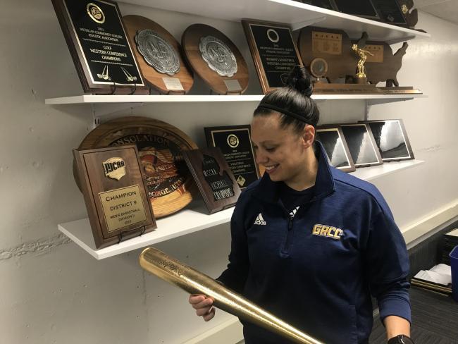 Whitney Marsh holding a golden Player of the Year bat in front of a trophy shelf.