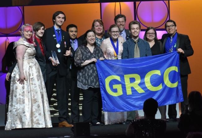Members of GRCC's Phi Theta Kappa chapter holds up a GRCC banner as they stand on a stage at the national conference.
