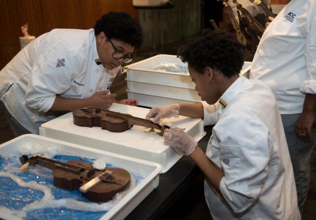 Students Kezia Stinson and Bryonna Farmer use chocolate to repair part of a violin.
