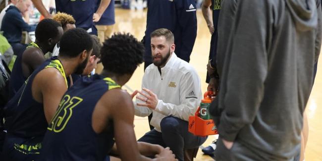 GRCC men's basketball coach Luke Bronkema kneeing during a break in the action, talking to his players.