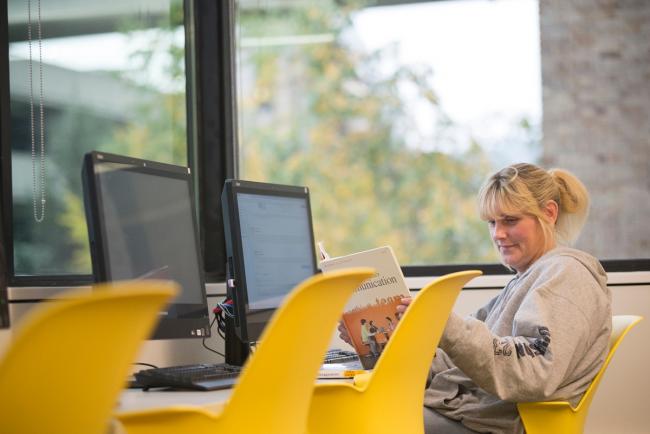 A female GRCC student sitting in a computer lab, looking at a text book.