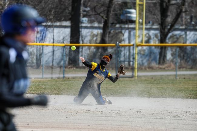 GRCC softball player throws from her knees to try and beat a runner headed to first base.