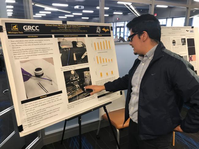 A TRIO student pointing to a display of his summer research from 2019.