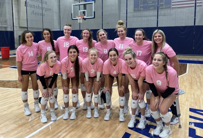 Volleyball players posing in their pink jerseys.