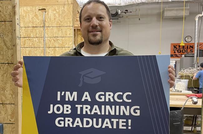 Martin Maloley holding a sign reading "I'm a GRCC Job Training Graduate"