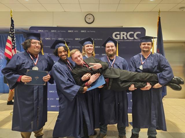 Assistant Professor Jonathan Wyckoff poses with GRCC Job Training program graduates holding him up in their arms.