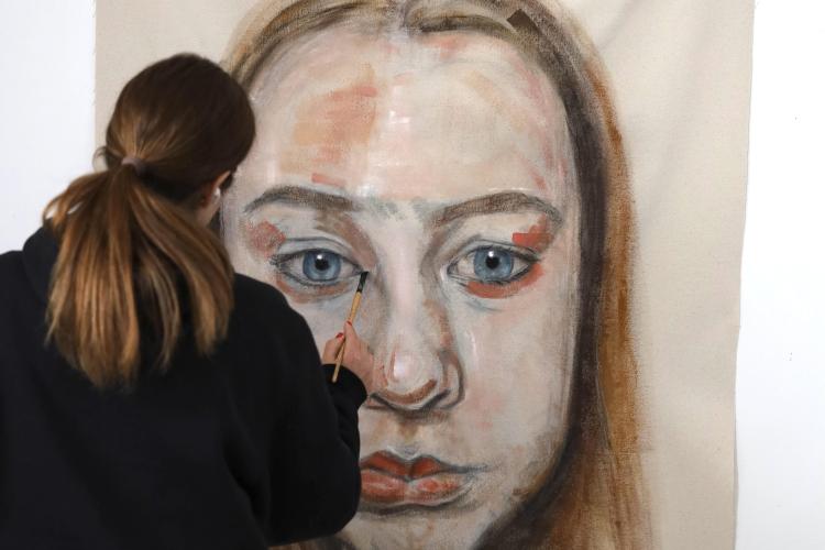 Erin Reinholz paints a face on a large canvas.