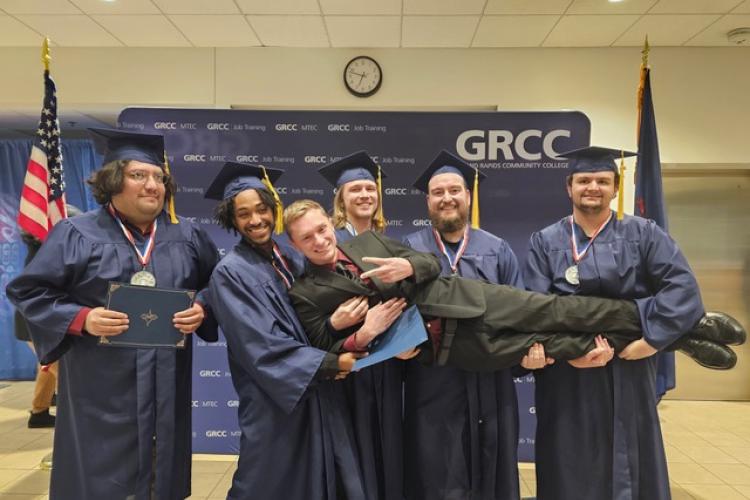 Assistant Professor Jonathan Wyckoff poses with GRCC Job Training program graduates holding him up in their arms.