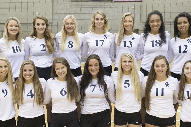 The 14 volleyball team members are in two rows in front of the net in the fieldhouse. The first row is kneeling.