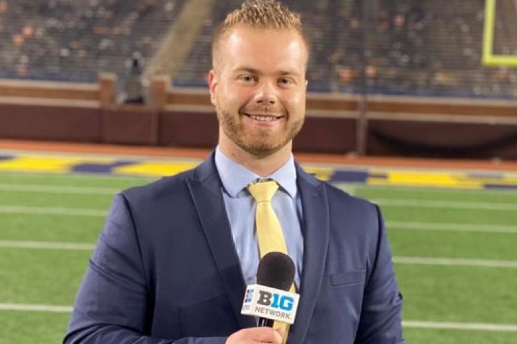 Amer posing with a microphone on the field at U of M.