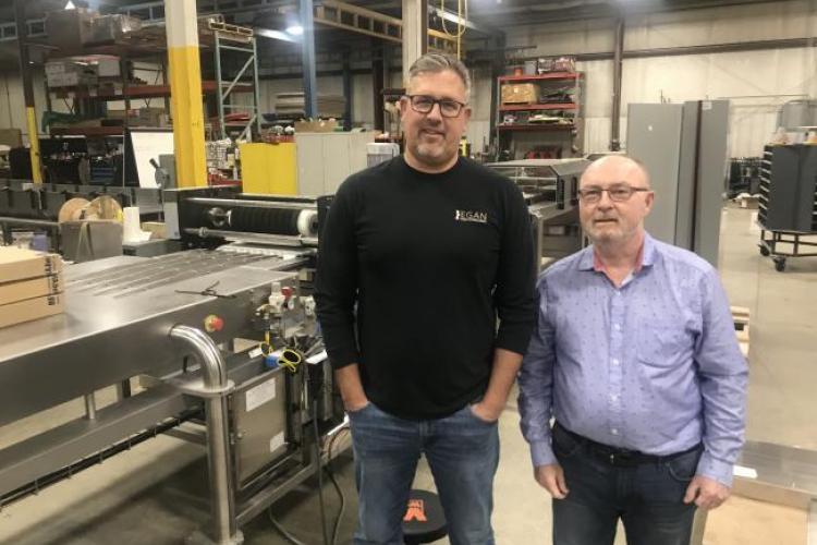 Mike Sherd and Bob Cisler stand near a machine they created to make candy.