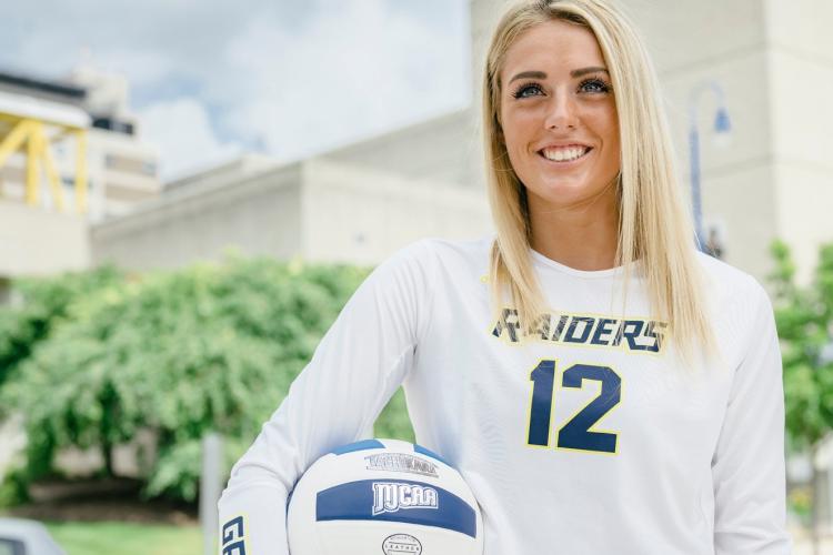 Portrait of Annie Holesinger in uniform holding a volleyball.