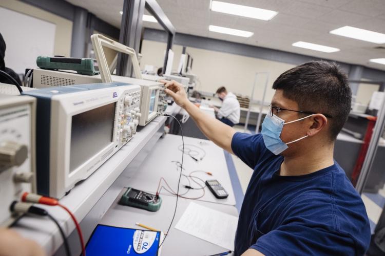 Student wearing a face covering working in an electronics lab.