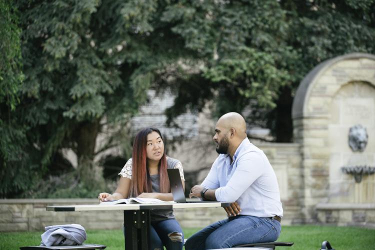 Students sitting at a table in the Olivarez Student Plaza with the fountain in the background.