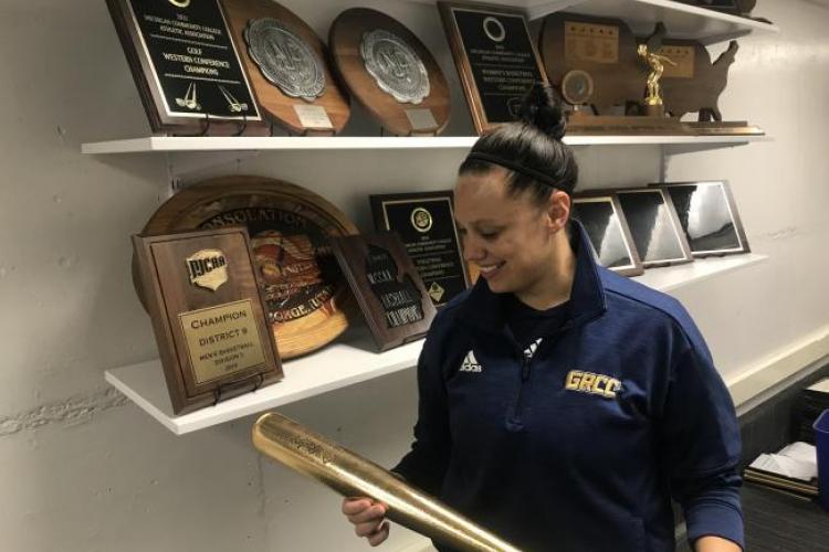 Whitney Marsh holding a golden Player of the Year bat in front of a trophy shelf.