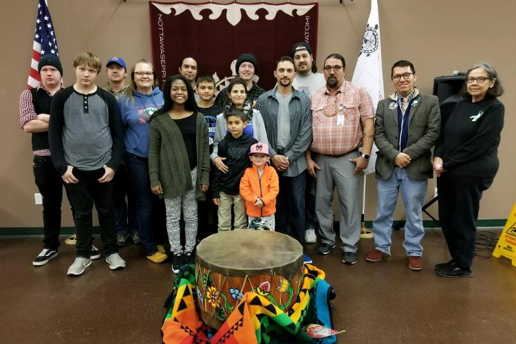 Sixteen people, include two little boys, stand behind a large drum.