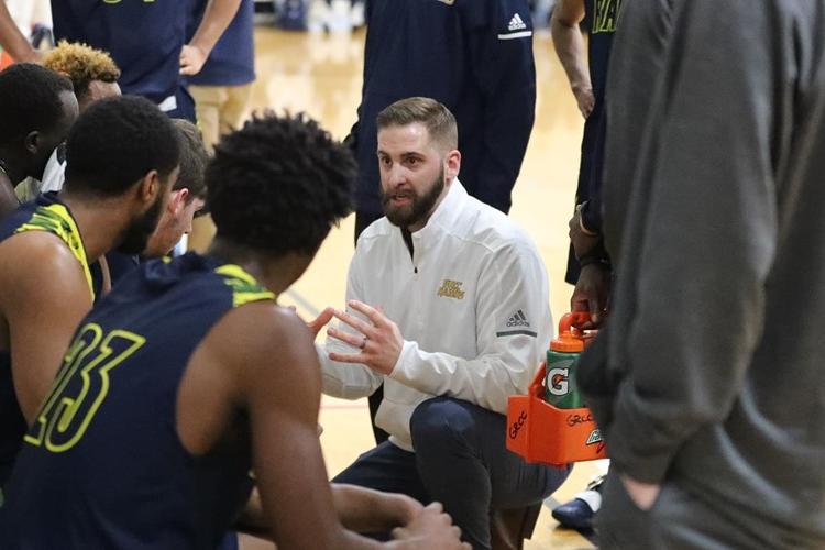 GRCC men's basketball coach Luke Bronkema kneeing during a break in the action, talking to his players.