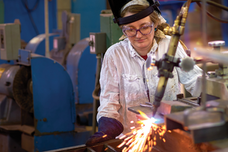 A female welding student working on a project, creating sparks