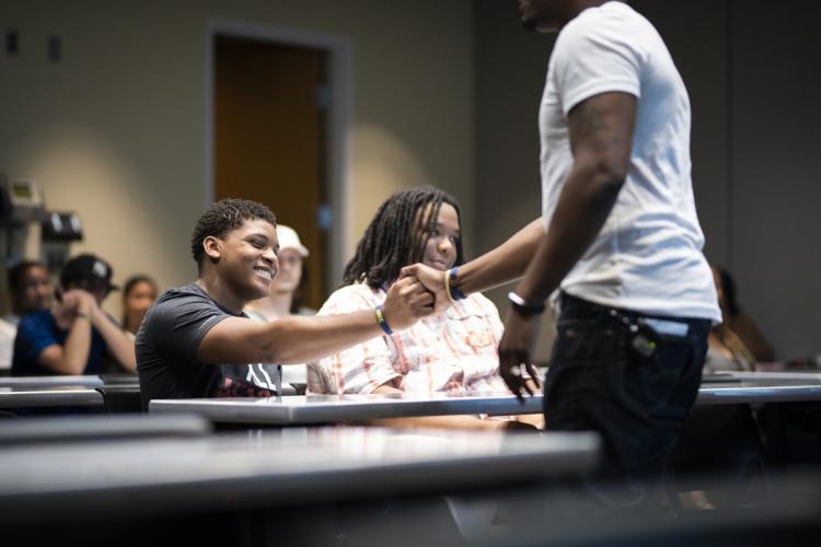 A student seated in a classroom shakes the hand of a presenter during Raider Nation Day.