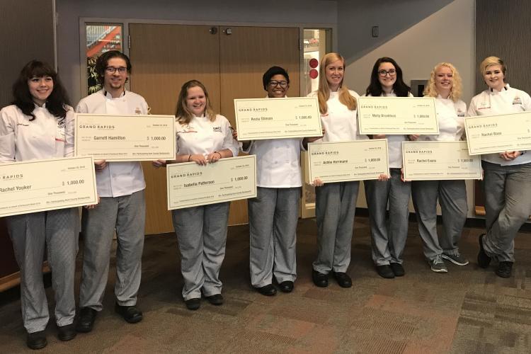 Eight culinary students hold up giant checks in front of the Heritage restaurant.