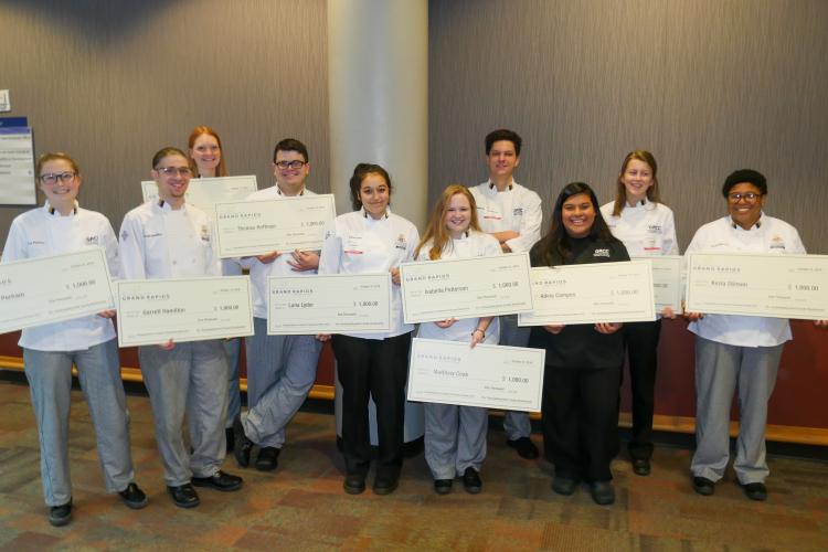 Culinary students hold up giant checks from Experience Grand Rapids.