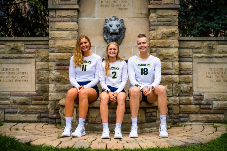 Sophomores volleyball players sitting by iconic lion fountain.