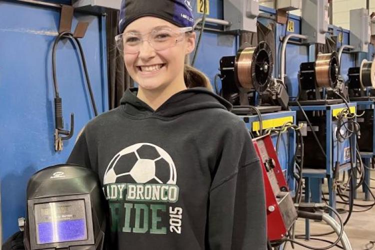 Andrea Ziebarth in the shop holding a welder's mask.