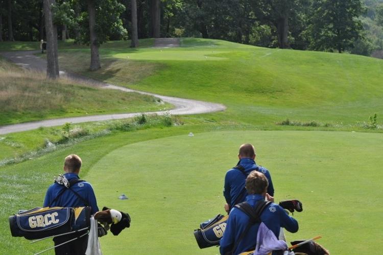 Three GRCC golfers, carrying their bags, walk onto a green.