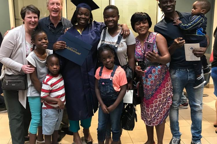 Valerie Wakam Kamsu, wearing a graduation cap and gown, holds up her Job Training certificate. She is surrounded by nine people.