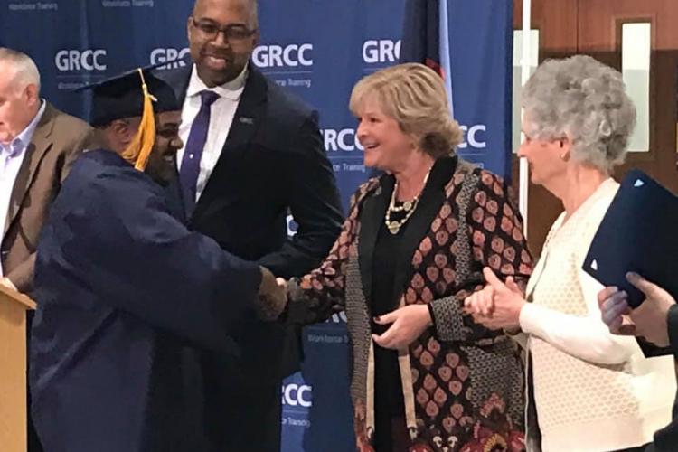 A Job Training graduate shakes Amy Mansfield's hand while Bill Pink and Cynthia Bristol look on.