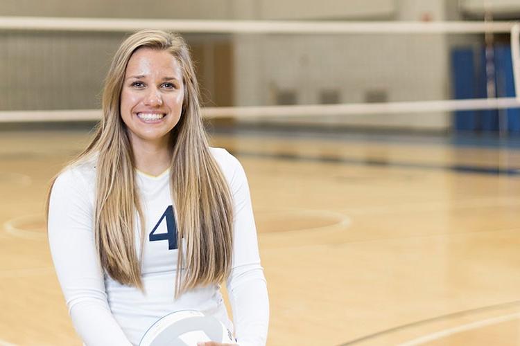 Lauren Helsen is next to the volleyball net in Ford Fieldhouse.