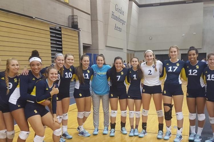 Volleyball team members stand in a row in the fieldhouse with their arms around each other.