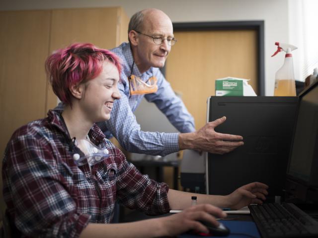 Student and professor laughing while working on a computer.