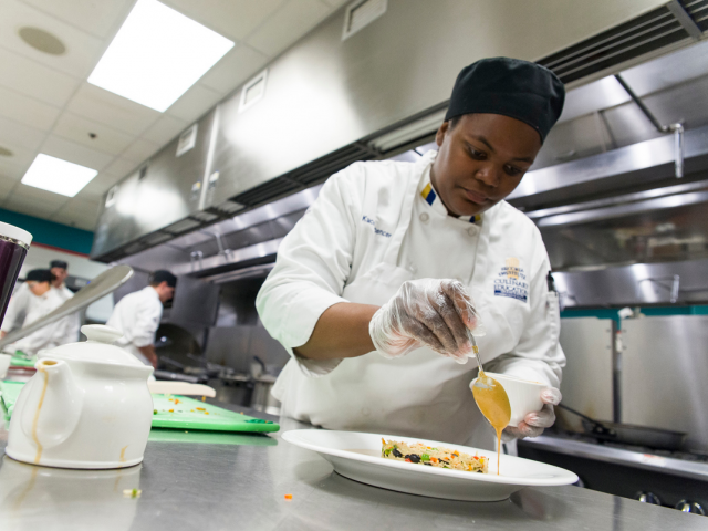 student sauces a plate in a culinary class.